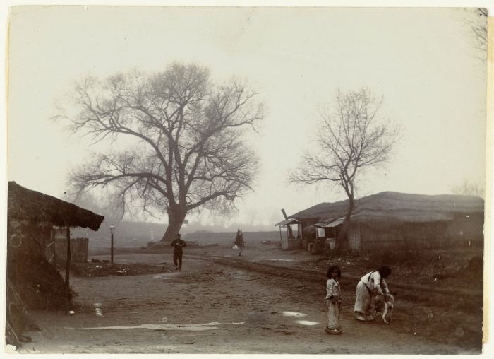 Jan Adriani: Twee kinderen spelen met een hond bij enkele huizen en twee wilgen, Pyongyang, Korea, 1907. Collectie Rijkmuseum